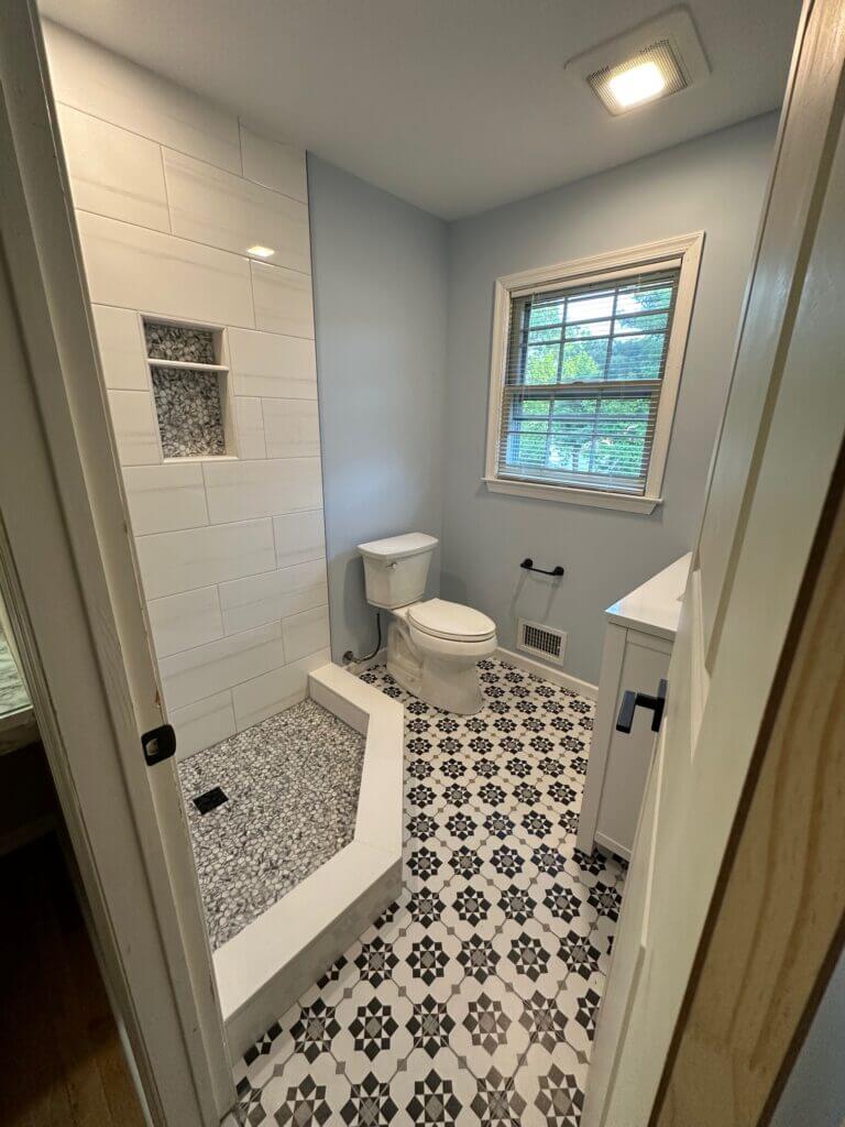 Walk-in shower with a pebble floor next to a patterned cement-look tile floor