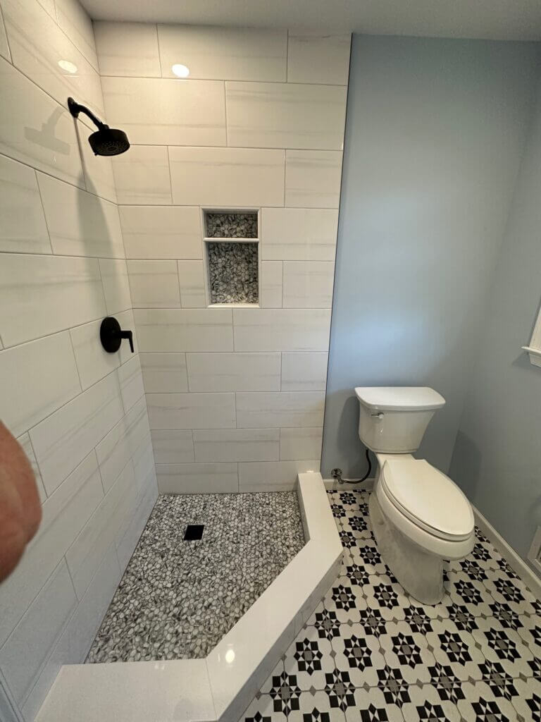 Walk-in shower with a pebble floor, tile niche and black fixtures