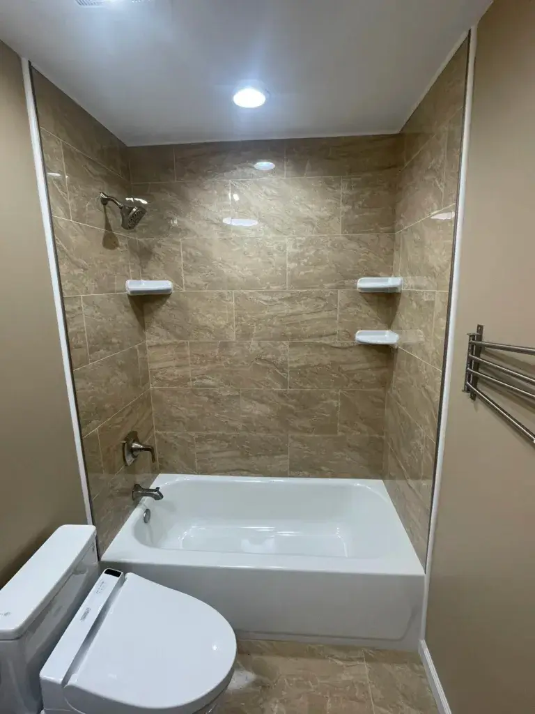 Bathtub with a beige stone-look tile surround and corner shelves