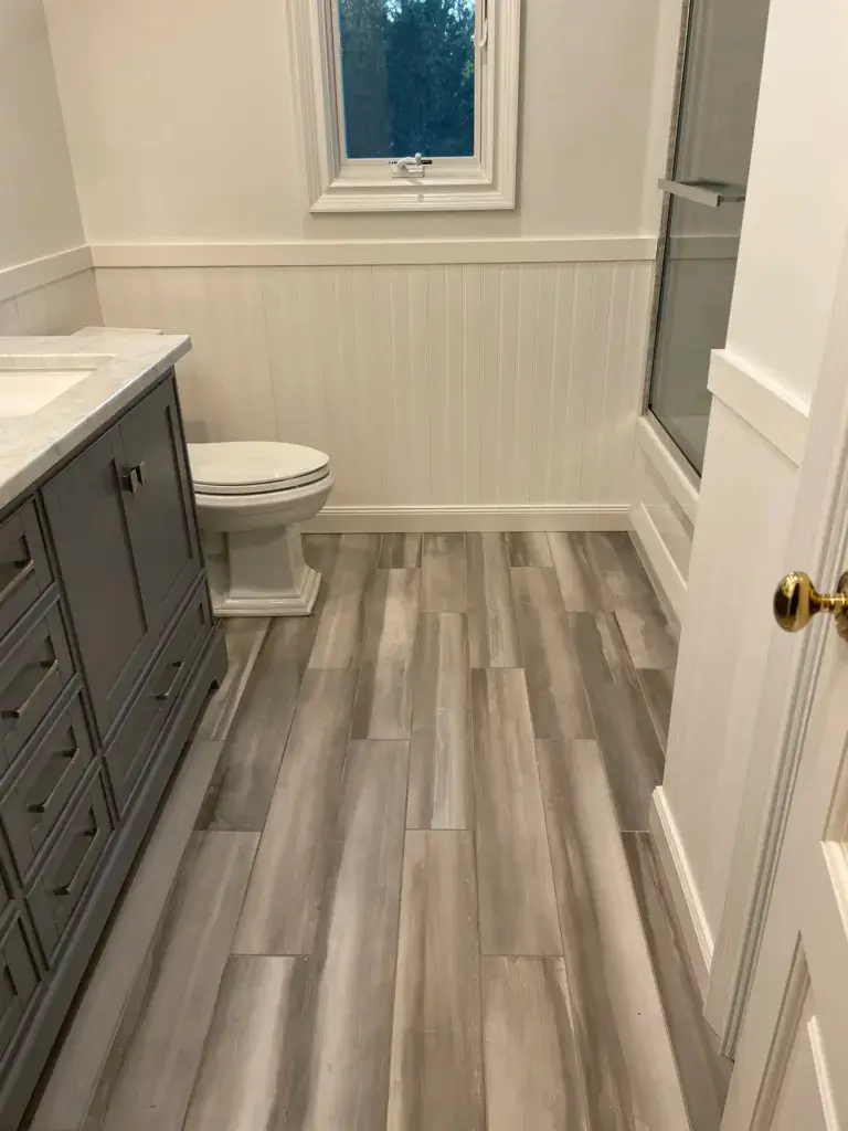 Bathroom with a gray vanity, white wainscoting and wood-look floor