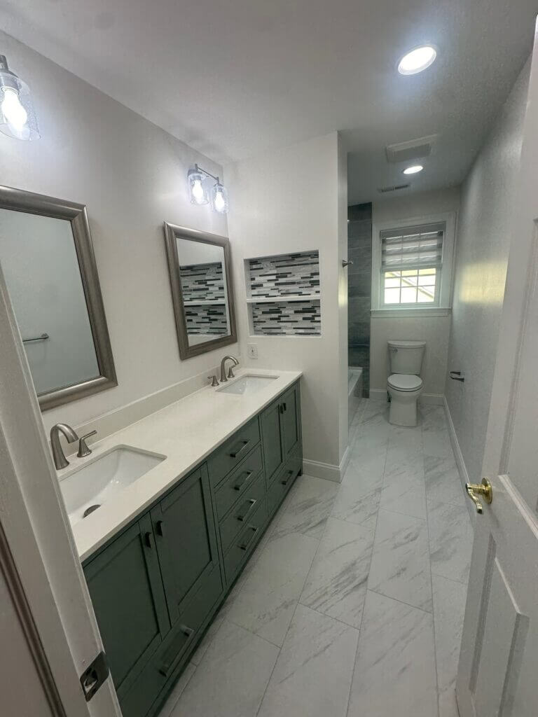 Remodeled bathroom with a double vanity, green cabinetry and marble-look tile flooring