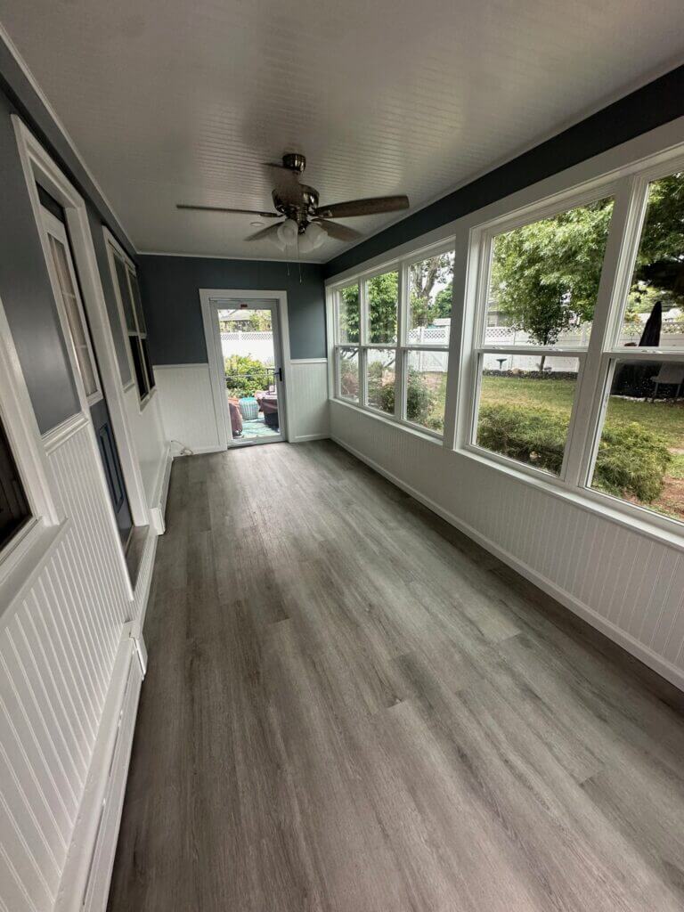 Enclosed sunroom with a wall of windows, plank flooring and a ceiling fan