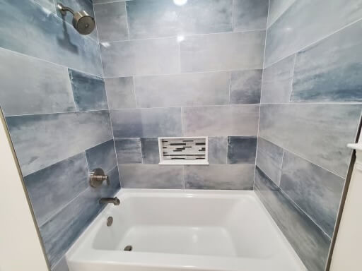 Remodeled bathroom with a marble-look tile tub surround and a recessed niche