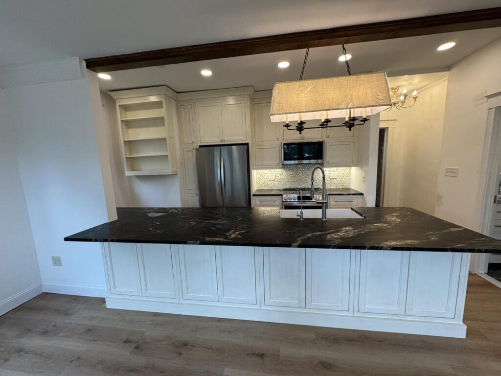 White kitchen remodel with a dark granite peninsula and an exposed wood beam