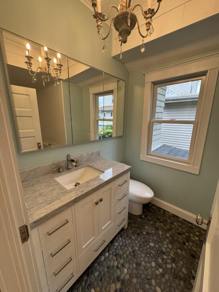 Bathroom with a cream vanity, stone counter, chandelier and river-rock tile floor