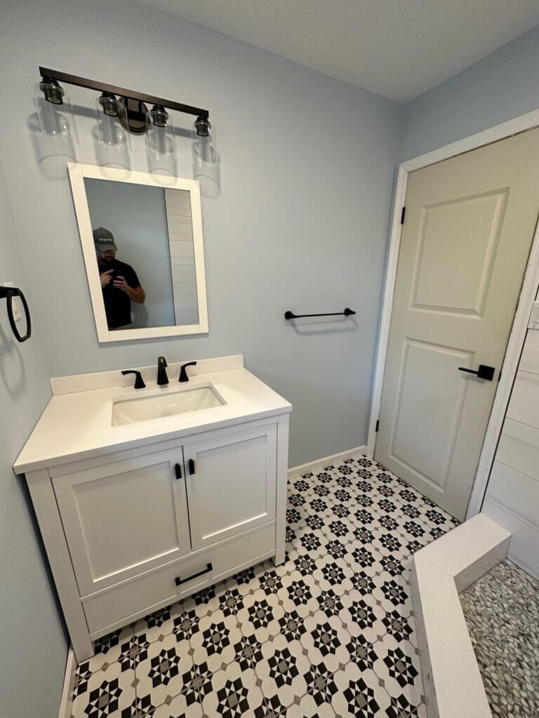 Remodeled bathroom with a white vanity, black fixtures and patterned floor tile