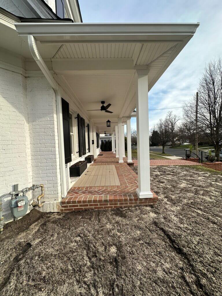 Long covered porch with white columns, a beadboard ceiling and a brick floor