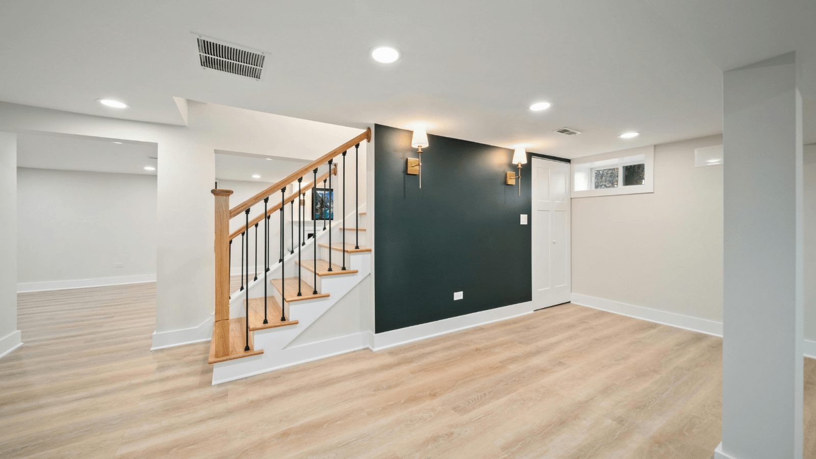 Finished basement with a dark green accent wall, oak staircase and wall sconces