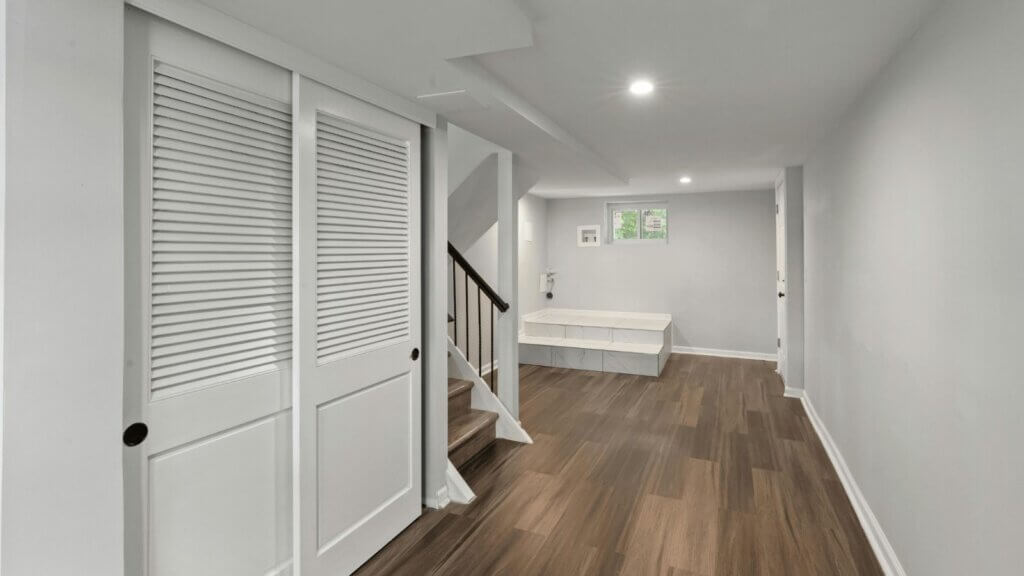 Finished basement hallway with louvered closet doors and plank flooring