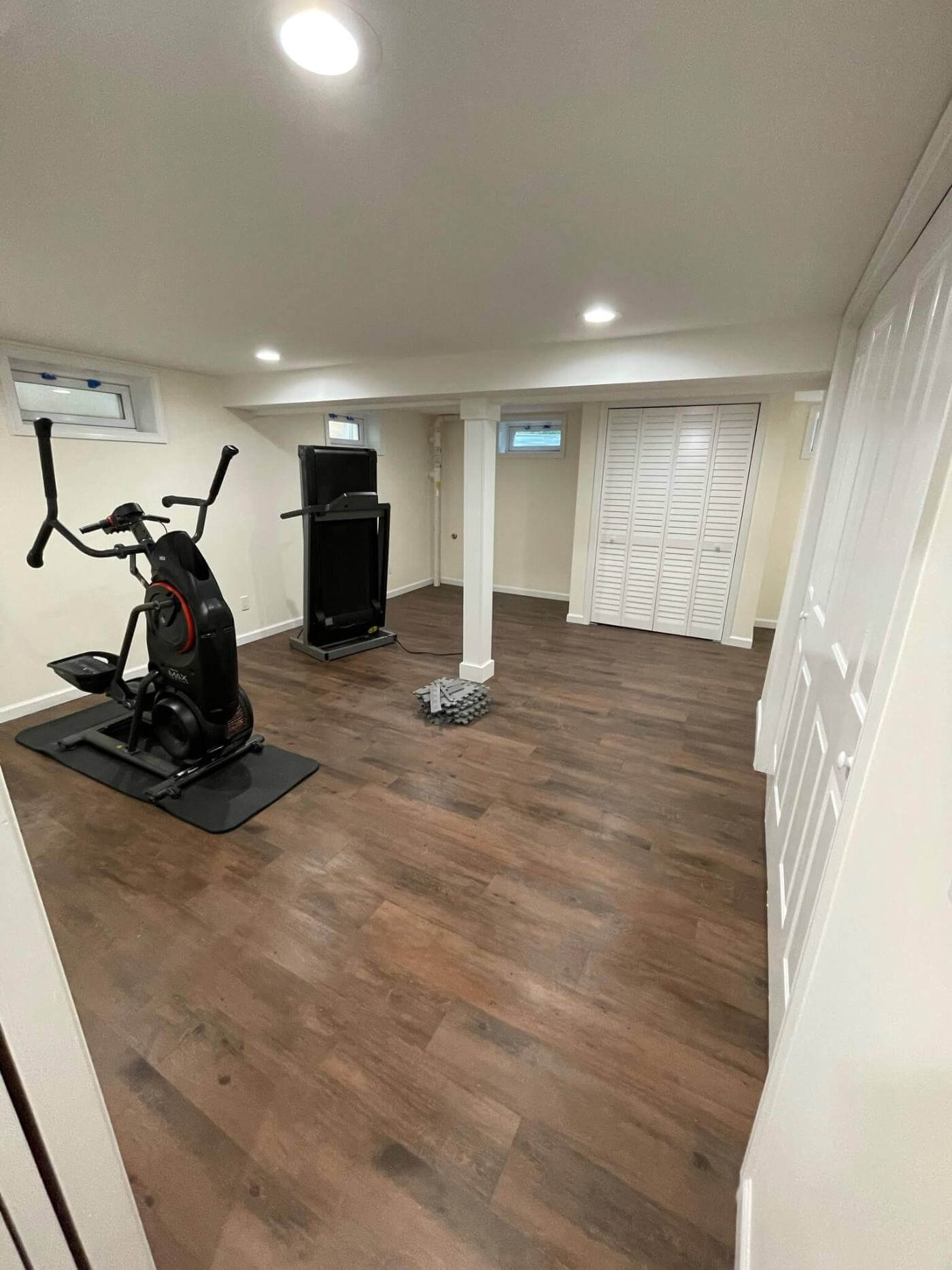Finished basement set up as a home gym with plank flooring and recessed lighting