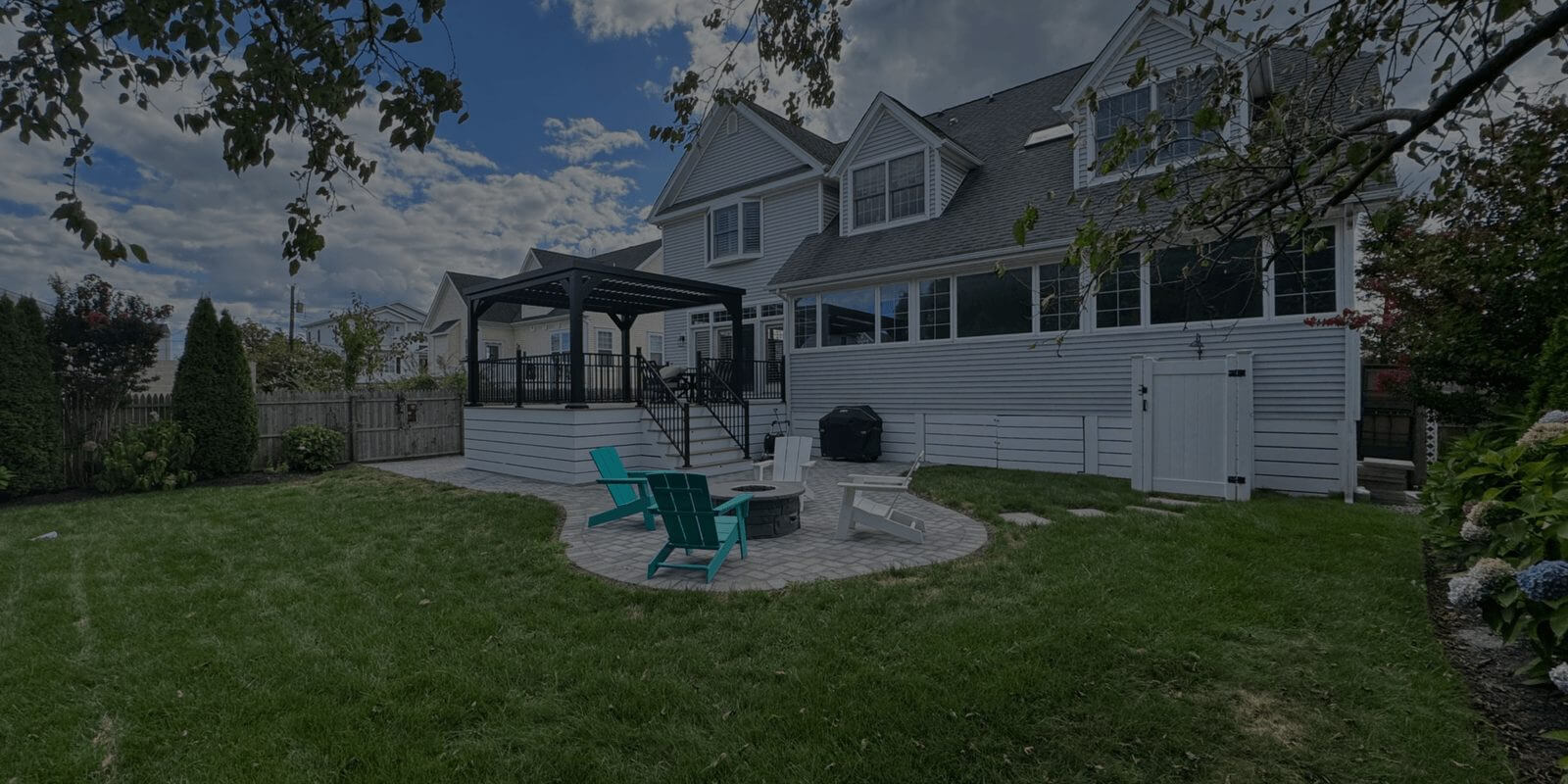 Backyard with a white pergola, fire pit and paver patio behind a shingled home